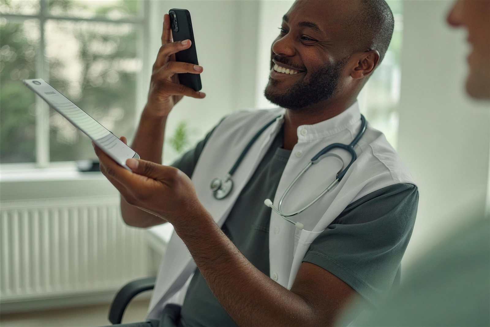 A UK doctor in a white coat with a stethoscope, using a phone to consult
